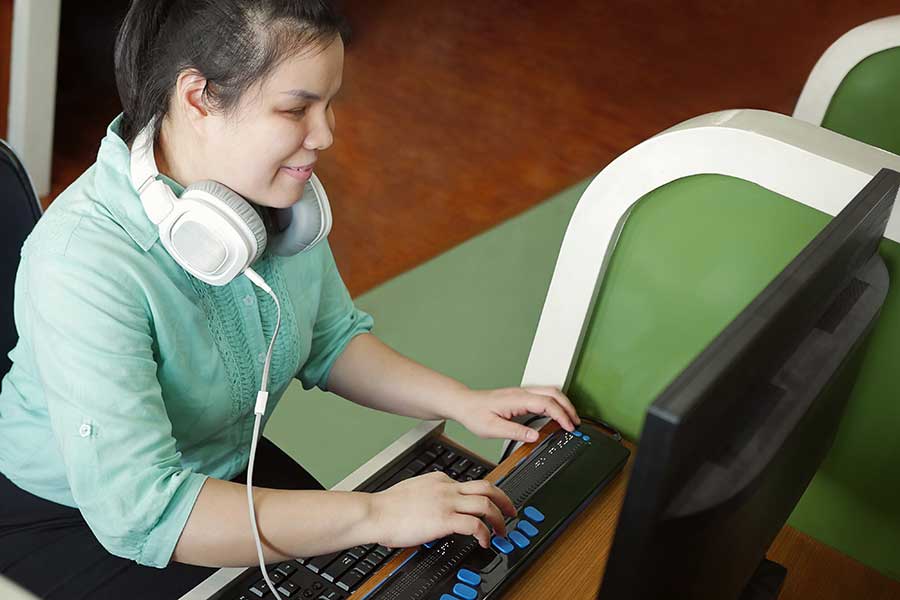 Person nutzt Screenreader mit Braille-Display an einem Laptop